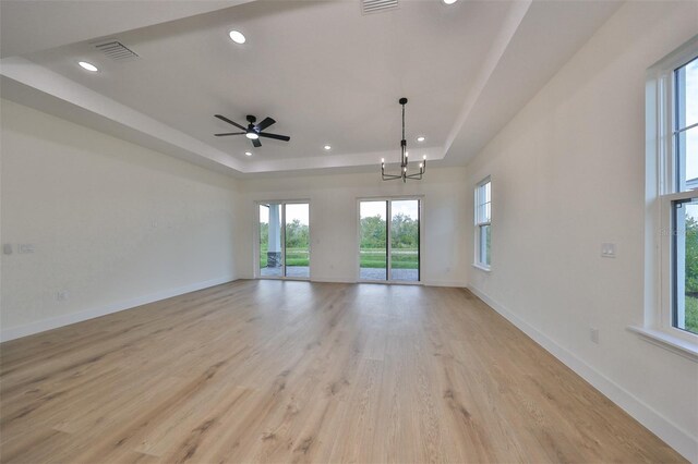 unfurnished room with ceiling fan with notable chandelier, light hardwood / wood-style floors, and a tray ceiling