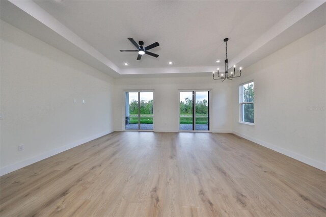 unfurnished room with ceiling fan with notable chandelier, light hardwood / wood-style floors, and a raised ceiling