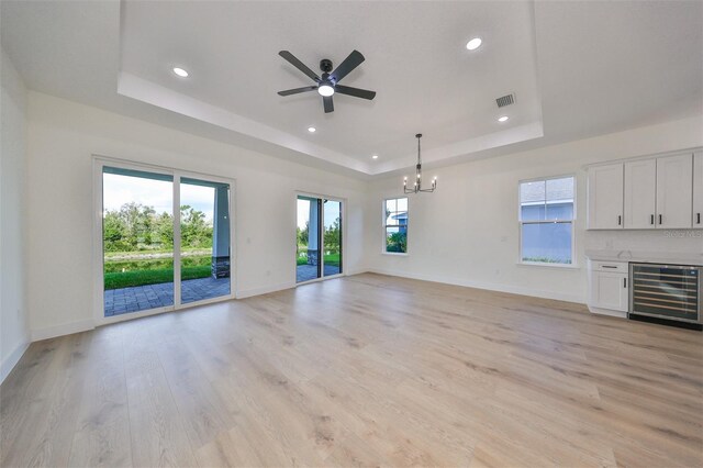 unfurnished living room featuring wine cooler, a raised ceiling, light hardwood / wood-style flooring, a fireplace, and ceiling fan with notable chandelier