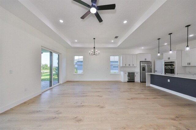 unfurnished living room featuring ceiling fan with notable chandelier, a tray ceiling, light hardwood / wood-style flooring, and wine cooler