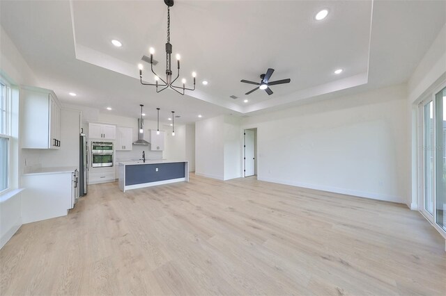 unfurnished living room with ceiling fan with notable chandelier, a tray ceiling, and a wealth of natural light