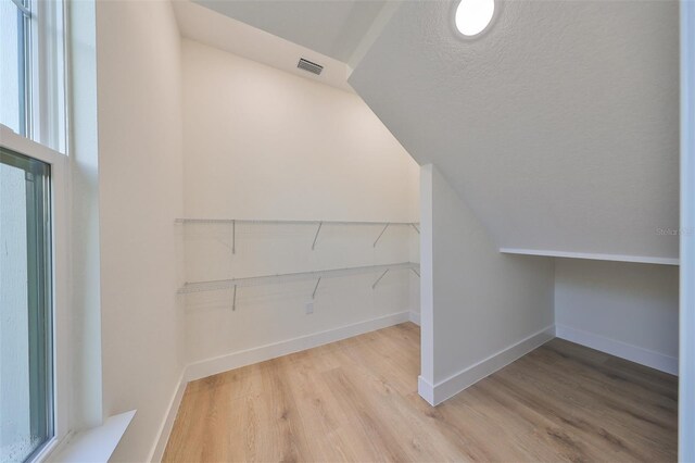 interior space featuring light wood-type flooring, vaulted ceiling, and a textured ceiling