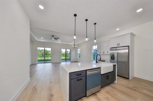 kitchen with light wood-type flooring, a kitchen island with sink, sink, white cabinetry, and appliances with stainless steel finishes