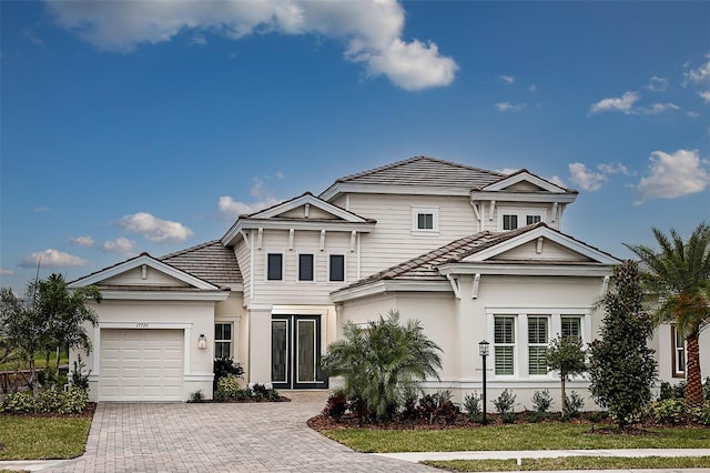 view of front facade featuring a garage, stucco siding, decorative driveway, and a tiled roof