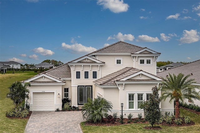 view of front facade featuring a garage, a tile roof, decorative driveway, a front yard, and stucco siding