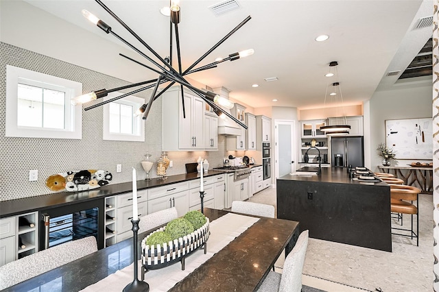 kitchen with an island with sink, stainless steel appliances, pendant lighting, sink, and white cabinets