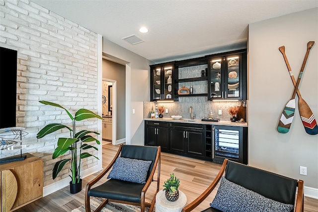 bar featuring visible vents, decorative backsplash, indoor wet bar, light wood-type flooring, and a sink