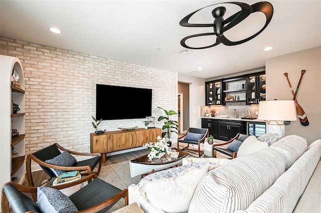 living room with indoor wet bar, visible vents, ceiling fan, brick wall, and wood finished floors