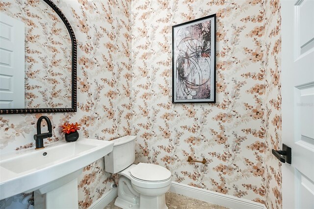 bathroom with baseboards, a sink, toilet, and wallpapered walls