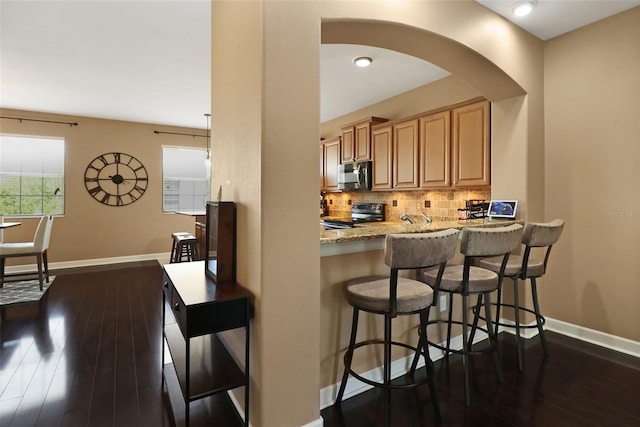 kitchen with backsplash, dark wood-type flooring, light stone counters, kitchen peninsula, and stainless steel appliances