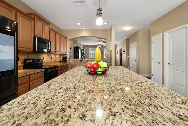 kitchen featuring decorative backsplash, light stone counters, ceiling fan, black appliances, and hanging light fixtures