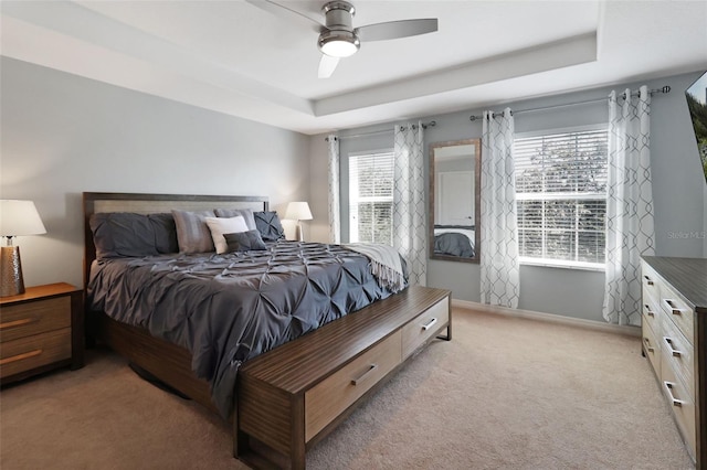 carpeted bedroom with a raised ceiling and ceiling fan