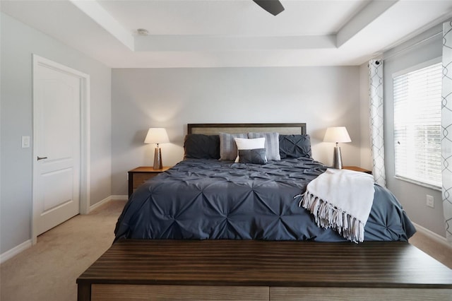 carpeted bedroom with a raised ceiling and ceiling fan