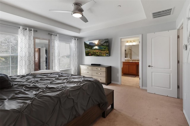 carpeted bedroom with a tray ceiling, ensuite bath, and ceiling fan