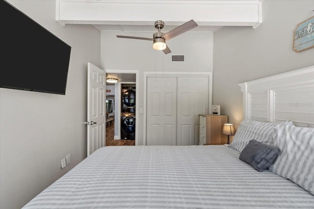 bedroom featuring a closet, ceiling fan, stacked washer / dryer, and beam ceiling