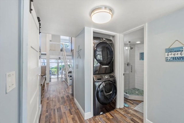 clothes washing area with a barn door, dark hardwood / wood-style floors, and stacked washer / drying machine