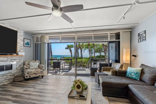 living room featuring a fireplace, a water view, hardwood / wood-style floors, ceiling fan, and floor to ceiling windows