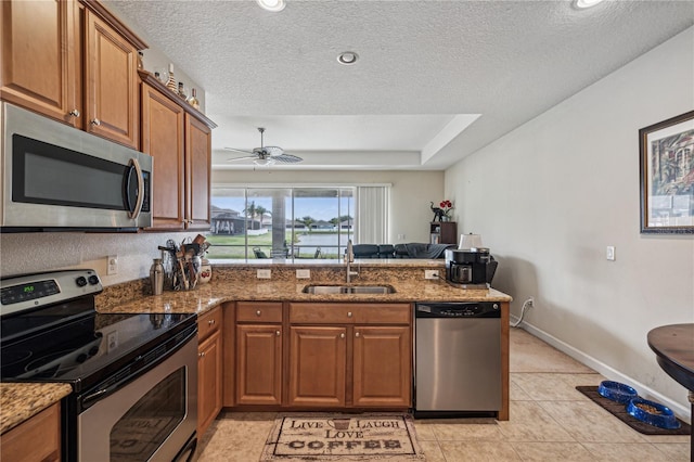 kitchen with appliances with stainless steel finishes, kitchen peninsula, sink, and stone counters