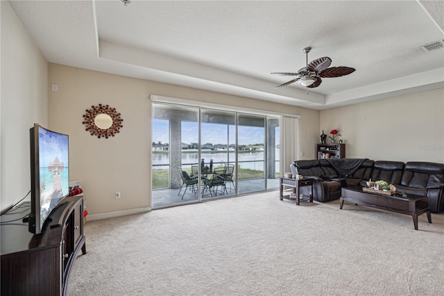 living room featuring carpet flooring, a water view, and a raised ceiling