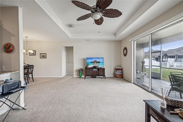 carpeted living room with a tray ceiling and ceiling fan with notable chandelier