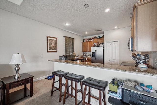 kitchen with stainless steel appliances, light stone counters, light carpet, and kitchen peninsula