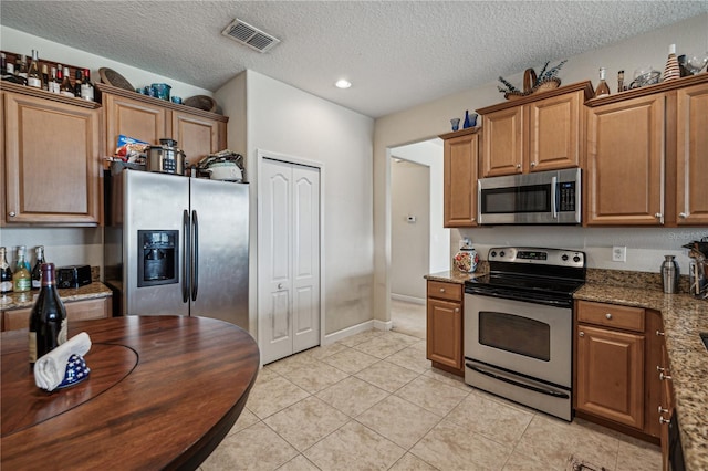 kitchen with a textured ceiling, light tile flooring, stone countertops, and stainless steel appliances