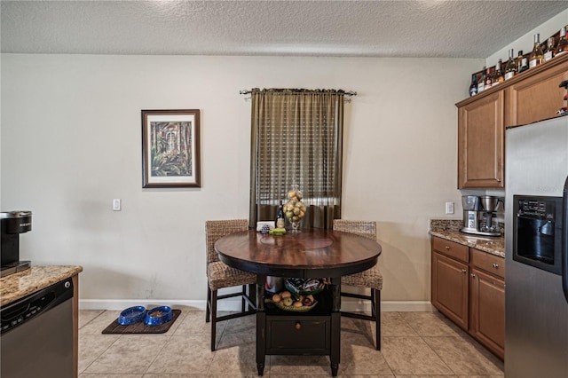 kitchen with a textured ceiling, stone countertops, light tile floors, and stainless steel appliances