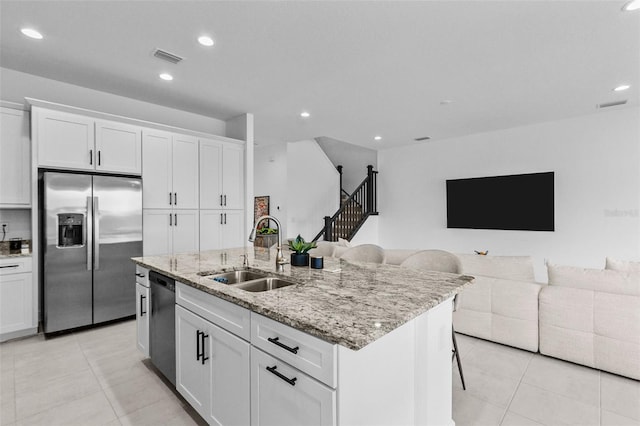 kitchen featuring light stone countertops, white cabinetry, sink, stainless steel appliances, and an island with sink