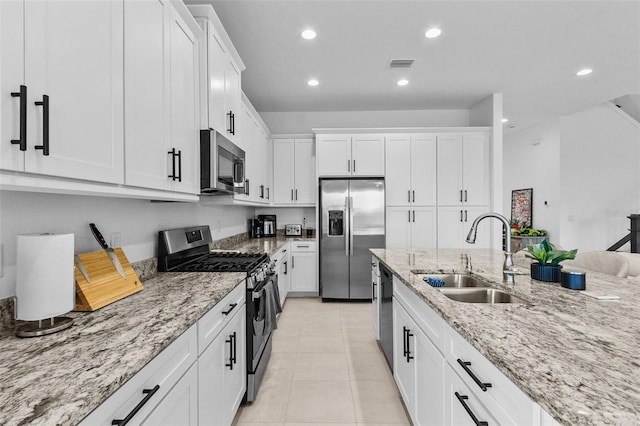 kitchen featuring light stone countertops, appliances with stainless steel finishes, sink, white cabinetry, and light tile patterned flooring