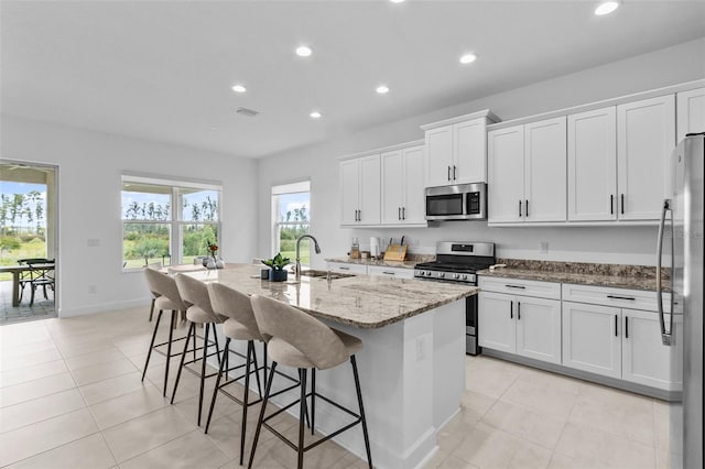 kitchen featuring light stone countertops, sink, stainless steel appliances, a center island with sink, and white cabinets