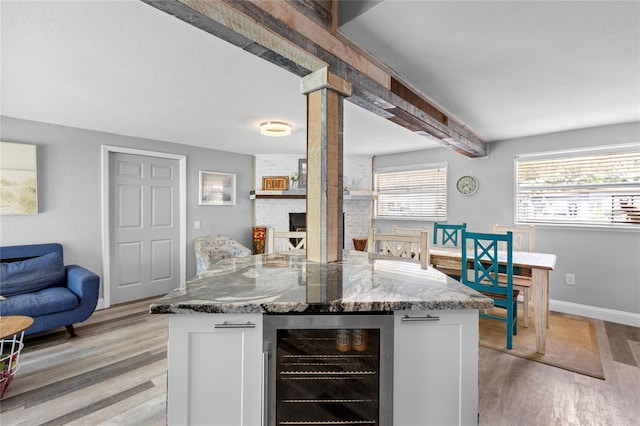 kitchen featuring light wood-type flooring, wine cooler, a brick fireplace, dark stone counters, and white cabinetry