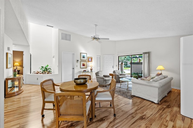 dining area with ceiling fan, high vaulted ceiling, light hardwood / wood-style floors, and a textured ceiling