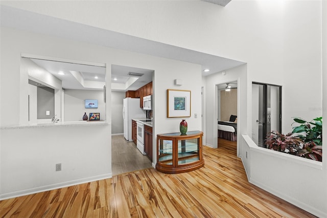 kitchen with white appliances, light hardwood / wood-style flooring, a raised ceiling, and ceiling fan