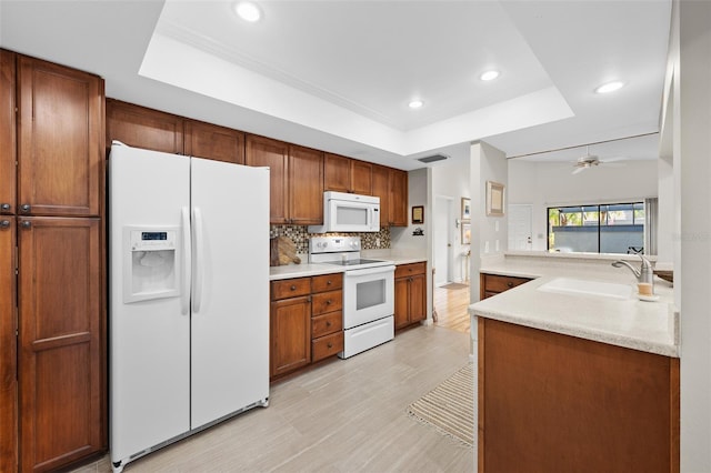 kitchen with a tray ceiling, kitchen peninsula, sink, and white appliances