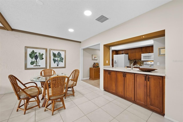 dining space featuring light tile patterned flooring, a textured ceiling, ornamental molding, and sink