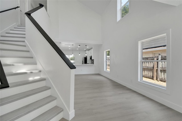 stairway with a wealth of natural light, a towering ceiling, and wood-type flooring