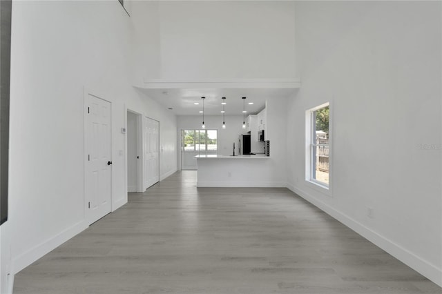 unfurnished living room featuring a towering ceiling, a healthy amount of sunlight, and light wood-type flooring