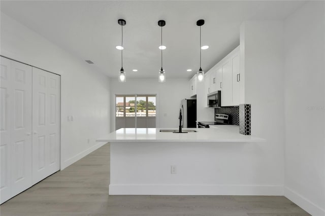 kitchen featuring pendant lighting, light hardwood / wood-style floors, kitchen peninsula, and stainless steel appliances