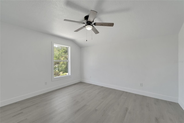 empty room with a textured ceiling, light wood-type flooring, vaulted ceiling, and ceiling fan