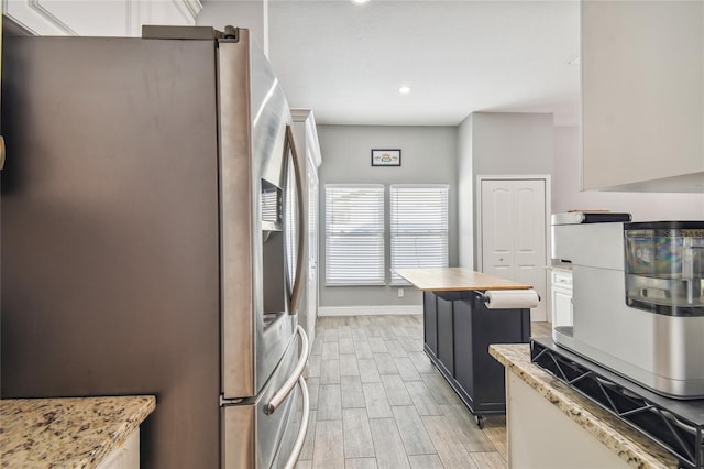 kitchen featuring white cabinetry, a center island, light stone countertops, and stainless steel refrigerator with ice dispenser