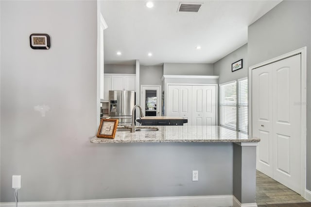 kitchen featuring light stone countertops, sink, kitchen peninsula, stainless steel fridge, and white cabinets