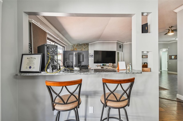 kitchen featuring hardwood / wood-style floors, lofted ceiling, a kitchen breakfast bar, ceiling fan, and ornamental molding