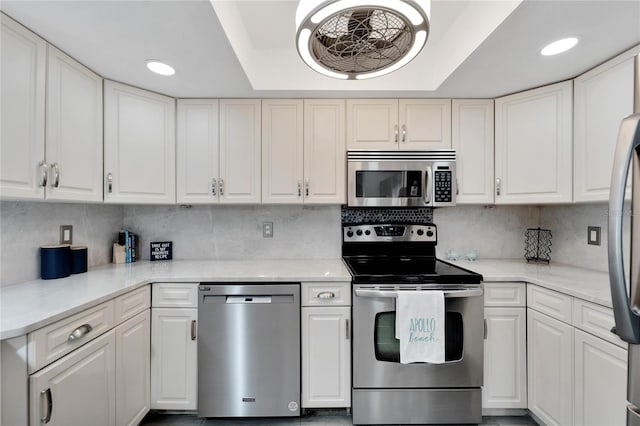 kitchen featuring a tray ceiling, decorative backsplash, white cabinets, and stainless steel appliances