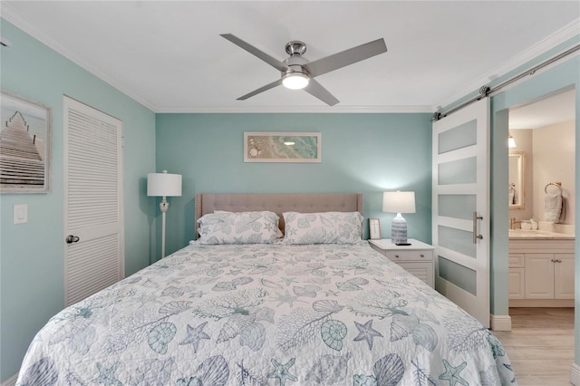 bedroom with ensuite bath, light hardwood / wood-style flooring, ceiling fan, a barn door, and a closet