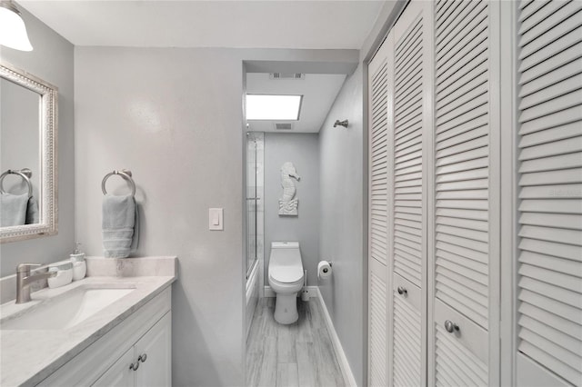 full bathroom featuring hardwood / wood-style flooring, vanity, combined bath / shower with glass door, and toilet