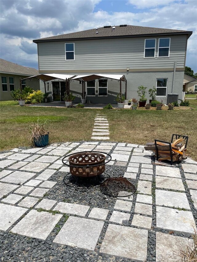 back of property with a fire pit, a patio area, and a yard