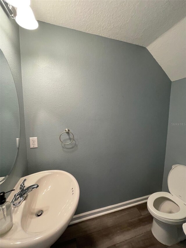 bathroom with lofted ceiling, sink, hardwood / wood-style flooring, toilet, and a textured ceiling