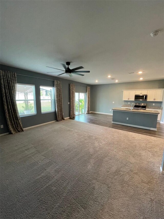 unfurnished living room featuring ceiling fan, sink, and carpet