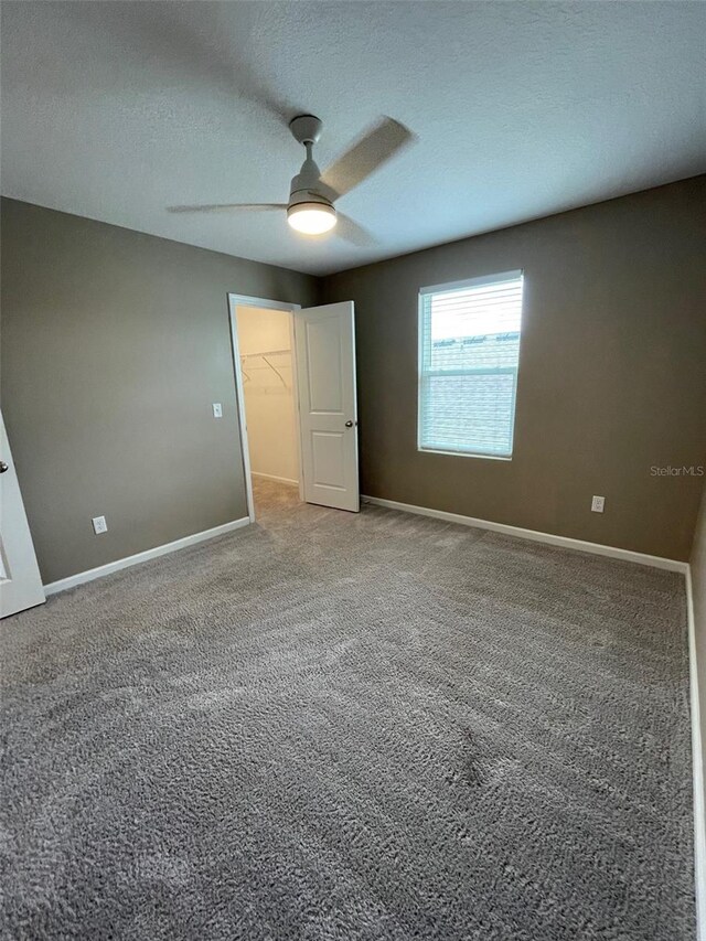 unfurnished bedroom with carpet, ceiling fan, a spacious closet, a textured ceiling, and a closet