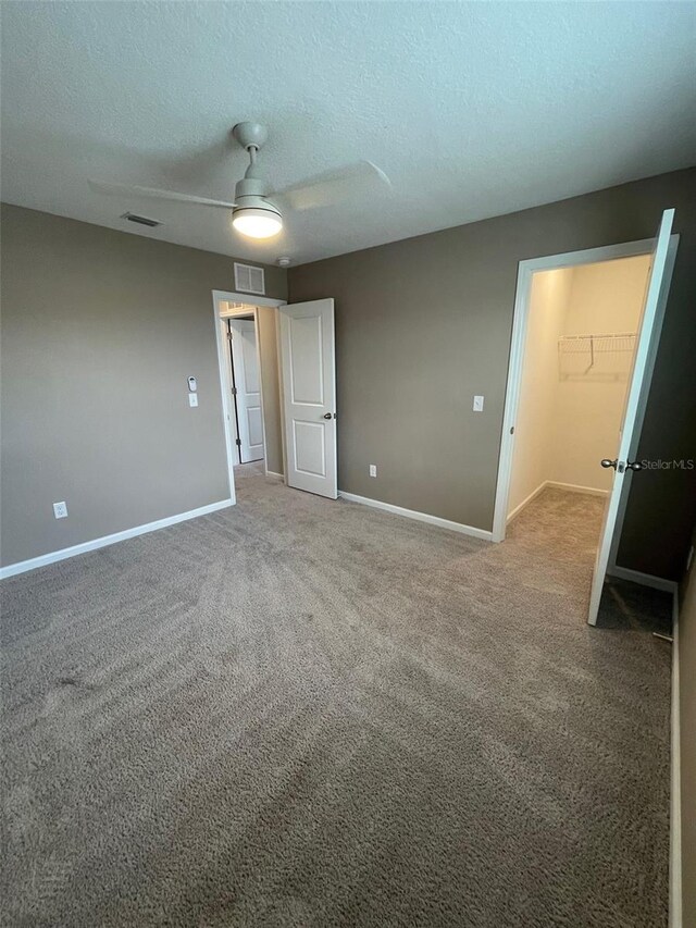 unfurnished bedroom with carpet, ceiling fan, a walk in closet, and a closet